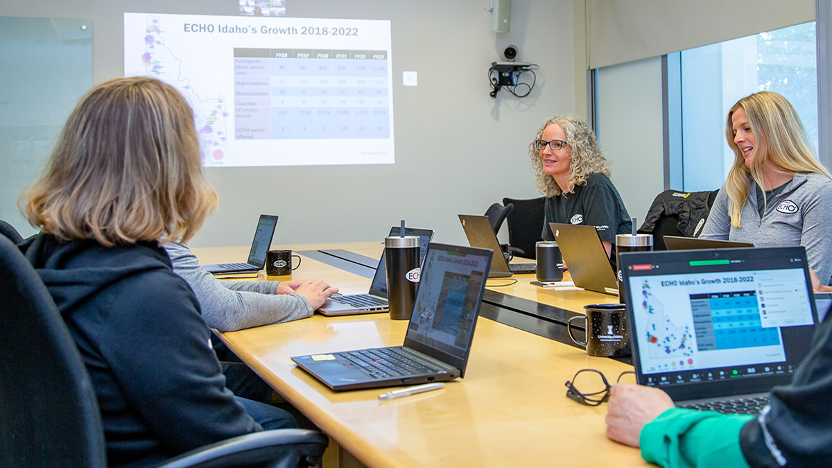 Five ECHO Idaho team members meeting in a conference room with laptops and a projection screen displaying information.