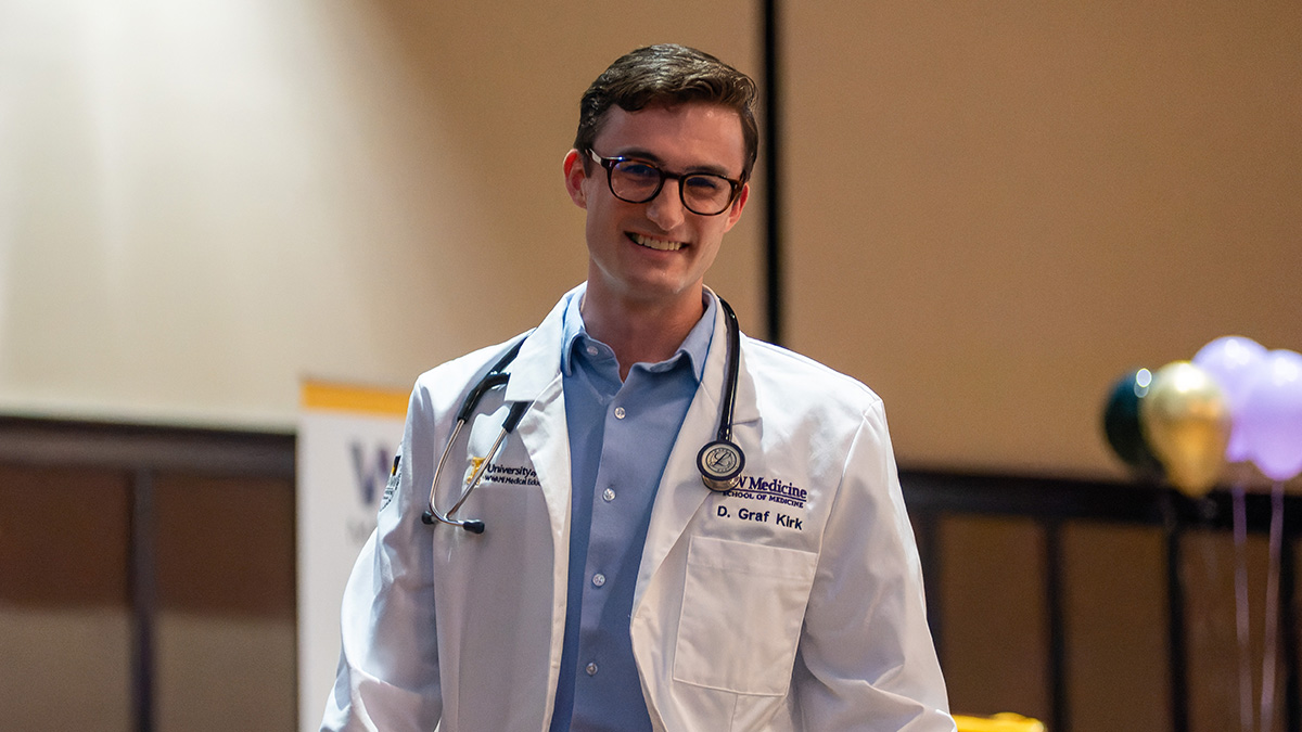 Medical student smiles wearing white lab coat and stethoscope.